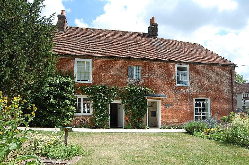 A charming red-brick house surrounded by greenery and flowers.